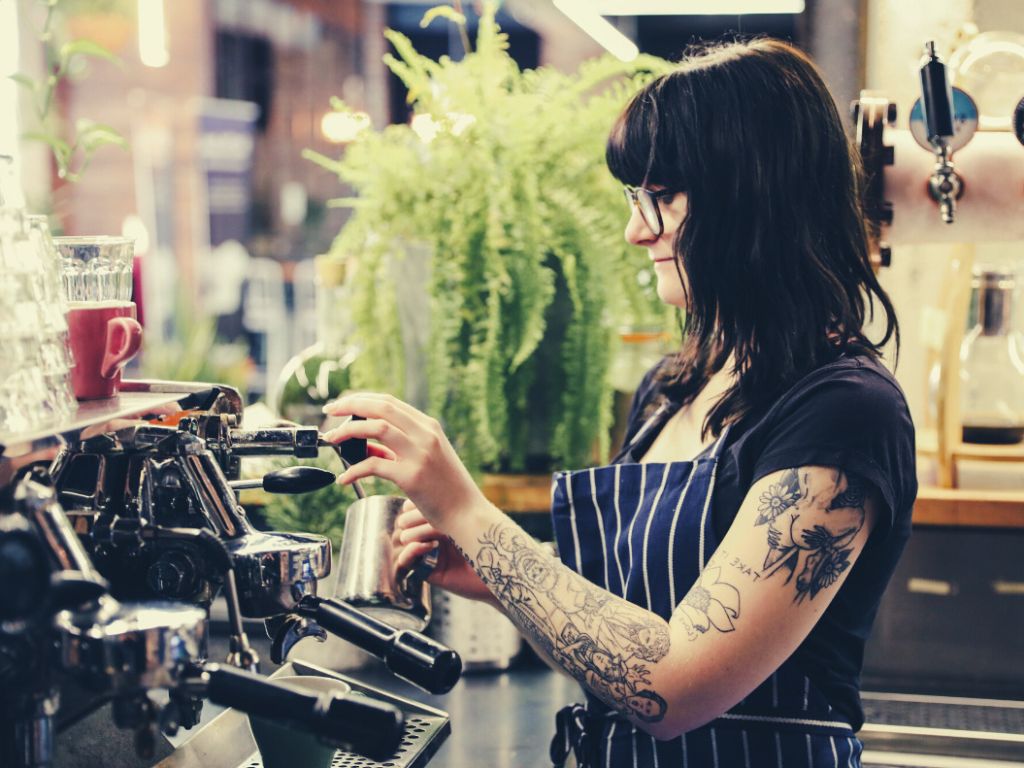 A barista with long hair and glassess operating the coffee machine