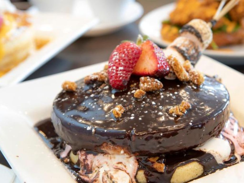 A small stack of three pancakes covered in melted chocolate and with strawberries on top.