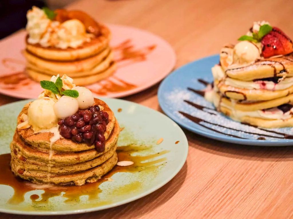 Three plates with small stacks of mini pancakes, each with different toppings.