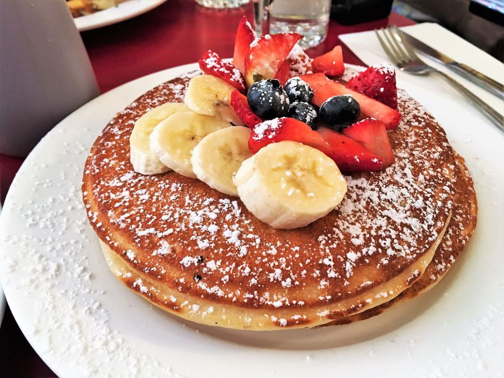 A small stack of three pancakes with icing sugar and berries on top.